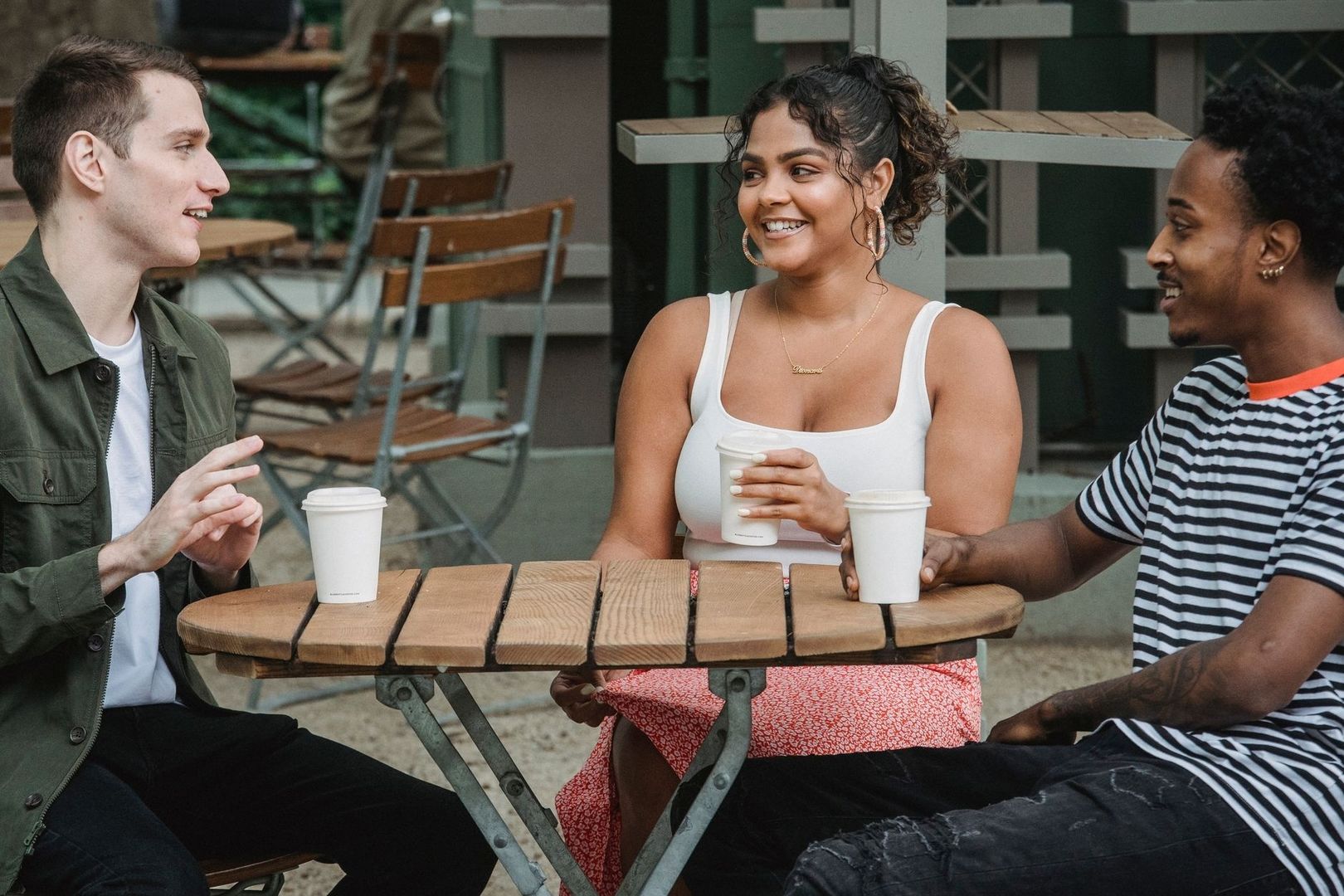 Tre personer samtalar över kaffe vid ett träbord på ett kafé