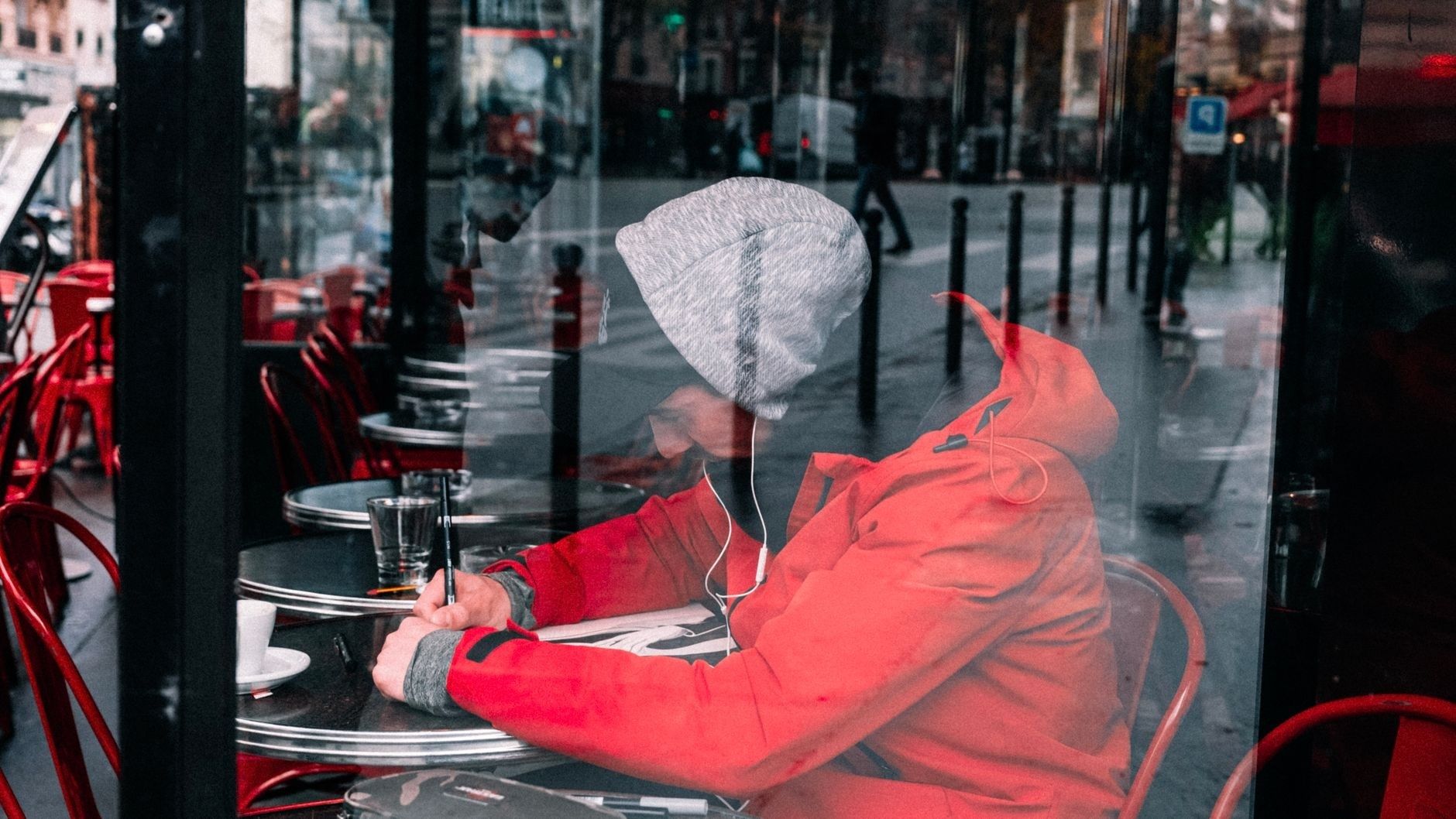 Person i röd jacka sitter på kafé och skriver med hörlurar på